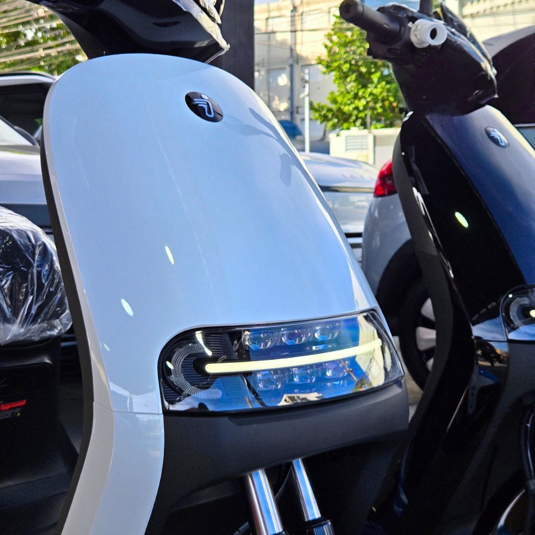 Ninebot E125 MK2 - Gris - Detalle frontal y faro. La unidad protagonista es gris claro, con componentes negros y detalles azules. Una segunda unidad negra aparece parcialmente al lado.